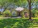 Charming single-story home featuring a red front door, lush landscaping, and mature shade trees at 1816 Curry Rd, Lutz, FL 33549