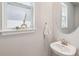Elegant half-bathroom with a pedestal sink, round mirror, and a decorative window with natural light at 31779 Asbury Ave, Wesley Chapel, FL 33545
