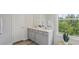 Modern bathroom with double sinks, gray cabinets, and a view of the outside scenery from the clear glass window at 32730 Winterwood Boulevard Blvd, Wesley Chapel, FL 33543