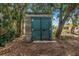 A weathered outbuilding with a pair of green doors is surrounded by trees and leaf debris at 5065 Shore Acres Ne Blvd, St Petersburg, FL 33703