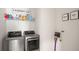 Modern laundry room featuring front loading washer/dryer and shelving with laundry necessities and decorative 'Wash and Dry' wall art at 8946 Ivy Stark Blvd, Wesley Chapel, FL 33545