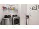 Modern laundry room featuring front loading washer/dryer and shelving with laundry necessities and decorative 'Wash and Dry' wall art at 8946 Ivy Stark Blvd, Wesley Chapel, FL 33545