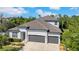 Beautifully landscaped, two-story home featuring a three car garage and manicured lawn with lush trees in the background at 7207 Peregrina Loop, Wesley Chapel, FL 33545