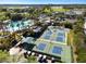 Aerial view of the community's six pickleball courts, a pool, a clubhouse, and palm trees at 2602 Novack Ct, Sun City Center, FL 33573
