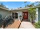 Inviting front entrance with wood decking and a red front door, surrounded by mature plants and large windows at 4765 Lake Valencia W Blvd, Palm Harbor, FL 34684