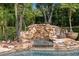 Close-up of the pool's rock waterfall feature with lush landscaping at 6352 W Maclaurin Dr, Tampa, FL 33647