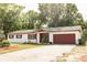 Exterior view of the home with a two car garage, a driveway, and a beautiful lush, tree-filled lawn at 12213 Floral Ln, Thonotosassa, FL 33592
