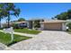 Home featuring a manicured lawn, mature landscaping, brick driveway, and a two-car garage at 13553 Glaze Brook Dr, Hudson, FL 34667