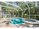 This backyard with screened-in pool area showcases a refreshing pool, hot tub, grill, and lush green trees at 12712 Stanwyck Cir, Tampa, FL 33626