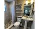 Bright bathroom with tiled shower, pedestal sink, open shelving, and natural light, showcasing a clean design at 1322 Idlewild Dr, Clearwater, FL 33755