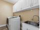 Laundry room with modern white appliances, overhead cabinets, a utility sink, and wood-look flooring at 10213 Lockwood Pines Ln, Tampa, FL 33635