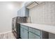 Modern laundry room with blue cabinets, stylish backsplash, and stainless steel washer and dryer at 1119 Hounds Run, Safety Harbor, FL 34695