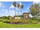 Stone community sign with decorative lighting surrounded by lush landscaping and towering palm trees at 2611 Eagle Crest Ct, Holiday, FL 34691