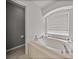 Bright bathroom featuring a soaking tub under an arched window and a commode at 27231 Liriope Ct, Wesley Chapel, FL 33544