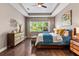 Comfortable bedroom featuring a tray ceiling, rich wood floors, a ceiling fan, and a large sunny window at 31050 Spruceberry Ct, Wesley Chapel, FL 33543