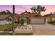 Inviting one-story home with a two-car garage and beautiful landscaping featuring flowers and palm trees at dusk at 4847 Harbor Woods Dr, Palm Harbor, FL 34683