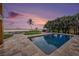 A beautiful pool with water view, mature trees, stone patio, and a fire pit sit under a colorful twilight sky at 8488 35Th N Ave, St Petersburg, FL 33710