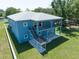 Aerial view of a two-story blue house, a covered porch, stairs, and a lush green lawn with surrounding trees at 1033 Hammock Cir, Tarpon Springs, FL 34688