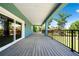 Covered back porch featuring gray wood flooring and black metal railings with a view of the landscaped yard at 1033 Hammock Cir, Tarpon Springs, FL 34688
