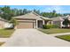 Single-story home with a manicured lawn, two car garage, and mature landscaping at 19528 Sunset Bay Dr, Land O Lakes, FL 34638