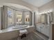 Luxurious bathroom featuring a large soaking tub with views to the pool, double sinks and tile floor at 12902 Grand Traverse Dr, Dade City, FL 33525