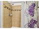 Close-up of a tiled shower with a shower head and decorative purple flower curtain at 13312 Waterford Castle Dr, Dade City, FL 33525