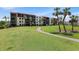 Condominium exterior showing a manicured lawn, mature palms, and a building with multiple screened balconies at 1935 Gulf Of Mexico Dr # G7-304, Longboat Key, FL 34228