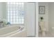 Bathroom boasts a unique glass block window, soaking tub, and modern fixtures, next to a toilet and closet at 3964 Silk Oak Ln, Palm Harbor, FL 34685