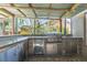 Covered outdoor kitchen featuring a stainless steel grill, bar area, fridge, and brick flooring at 9112 Calle Alta, New Port Richey, FL 34655