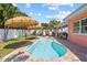 Sparkling kidney-shaped pool with thatched umbrellas, surrounded by patio and greenery at 10448 Hetrick W Cir, Largo, FL 33774