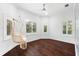 Serene bedroom with a hanging chair, three shuttered windows, hardwood floors, and neutral decor at 1600 Magnolia Rd, Belleair, FL 33756