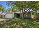 Inviting single-Gathering home featuring a manicured lawn, mature tree, and two-car garage at 1393 Chesterfield Dr, Dunedin, FL 34698