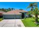 Charming single-story home featuring a three-car garage, a well-manicured lawn, and mature palm trees at 2321 Wood Pointe Dr, Holiday, FL 34691