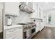 Close up of modern kitchen with stainless steel range, white cabinets, marble backsplash, and custom range hood at 2604 S Bryant Cir, Tampa, FL 33629