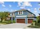 Inviting two-story blue home showcasing a three-car garage and beautifully landscaped front yard under a bright blue sky at 10017 Smarty Jones Dr, Ruskin, FL 33573