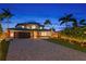 Beautiful two-story home showcasing brick driveway, mature palm trees, manicured landscaping, and an illuminated exterior at 2250 Donato Dr, Belleair Beach, FL 33786