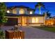 Charming two-story home displaying a brick driveway, tropical landscaping, and inviting exterior lighting at twilight at 2250 Donato Dr, Belleair Beach, FL 33786