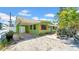 Exterior of the charming green home with red shutters and a covered carport, surrounded by lush greenery under a blue sky at 121 86Th Ter, Treasure Island, FL 33706
