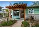 Inviting entryway featuring a light wood pergola, wooden door with glass panels and lush landscaping at 3962 Poinsettia Dr, St Pete Beach, FL 33706