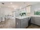 Bright, open kitchen features gray cabinetry, quartz countertops, and stainless steel appliances, adjoining a sunlit living space at 7402 America Way, New Port Richey, FL 34654