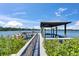 Wooden walkway leading to a covered boat dock with lifts, surrounded by lush greenery and open water at 935 Chipaway Dr, Apollo Beach, FL 33572
