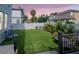 Backyard at twilight features artificial turf, tropical plants, and a white fence, enhancing privacy and charm at 2707 W Fig St, Tampa, FL 33609