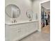 This bathroom features double sinks, white cabinets and matching round mirrors that lead to a well-organized closet at 2707 W Fig St, Tampa, FL 33609