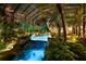 Nighttime view of the pool featuring rock waterfalls, lush tropical landscaping, and a screened enclosure at 11865 Fort King Hwy, Thonotosassa, FL 33592
