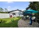Landscaped backyard with stone, lush lawn, and an outdoor seating area with an umbrella for shade at 14702 Dartmoor Ln, Tampa, FL 33624