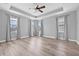 Main bedroom featuring tray ceilings, a ceiling fan, three windows, and stylish wood-look flooring at 14718 Rocky Brook Dr, Tampa, FL 33625