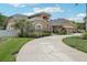 A tan two-story home featuring a curved driveway, an arched entryway, and a three-car garage, with mature landscaping at 16910 Equestrian Trl, Odessa, FL 33556