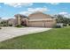A tan two-story home featuring a curved driveway, an arched entryway, and a three-car garage, with mature landscaping at 16910 Equestrian Trl, Odessa, FL 33556