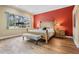Bright main bedroom featuring hardwood floors, a red accent wall, and a large window at 5132 Pinnacle Dr, Oldsmar, FL 34677