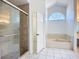 Bright bathroom featuring tiled floors, a soaking tub under an arched window, and a glass-enclosed shower at 1005 Cameo Crest Ln, Valrico, FL 33596
